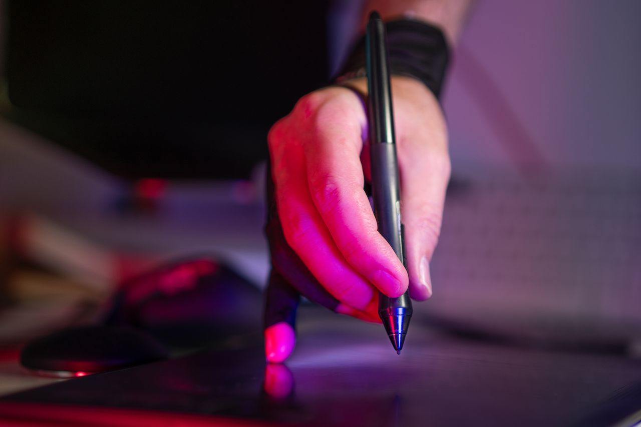 hero-img-02 A digital artist's hand working on a graphics tablet with a stylus, in a creative studio setting.